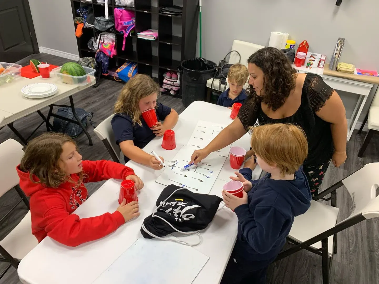 Children work at a table while a helper leans in beside them