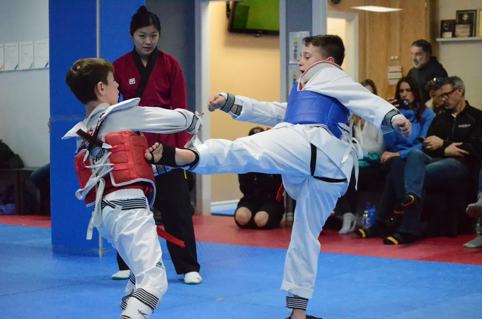 Two young students spar in chest protectors while parents watch