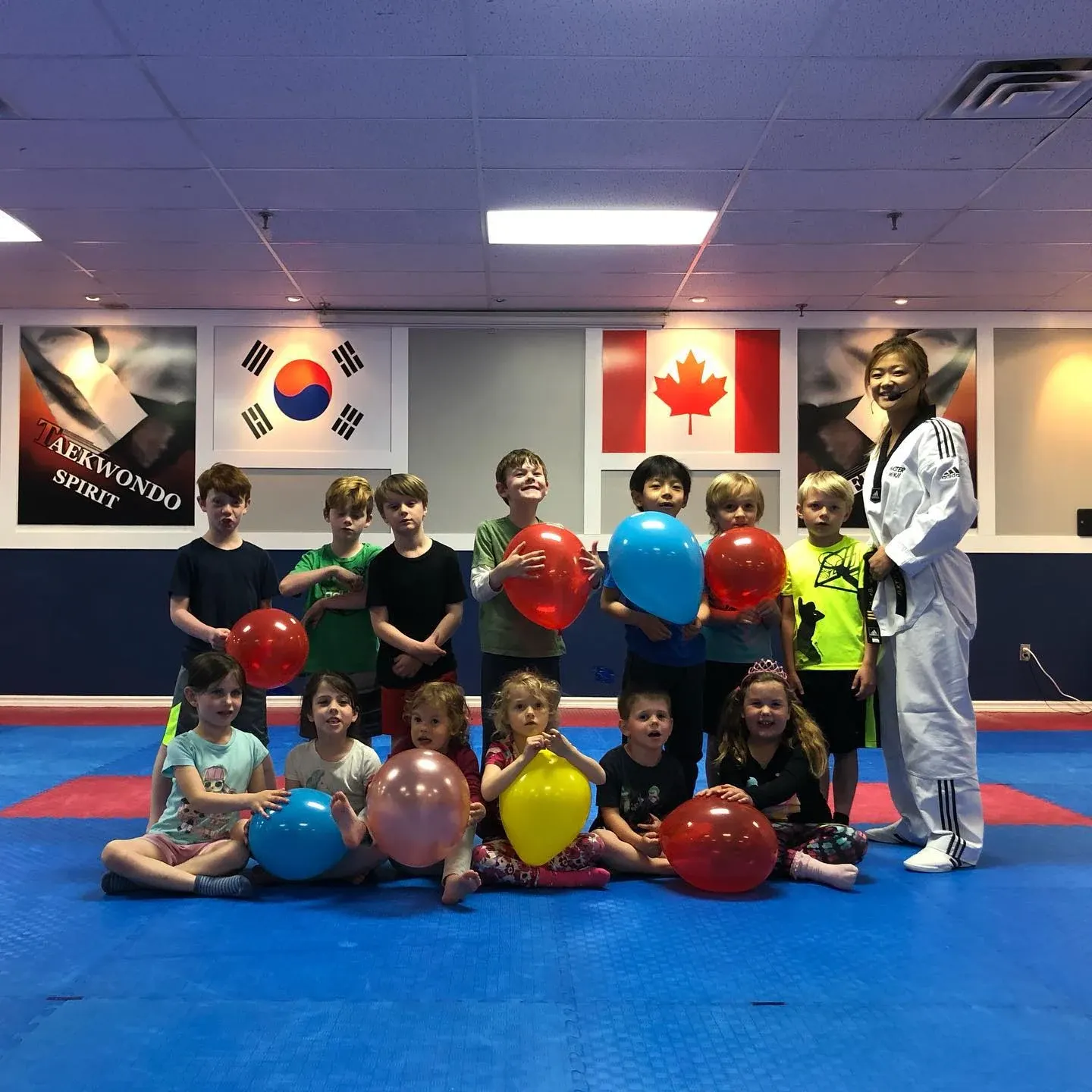 Children hold red, blue and yellow balloons on the mat beside an instructor