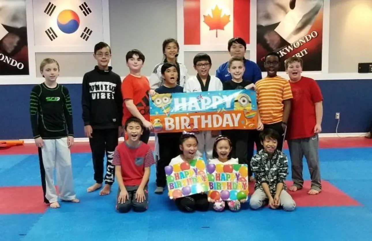 Birthday guests hold up Happy Birthday signs on the mats, with two instructors behind them