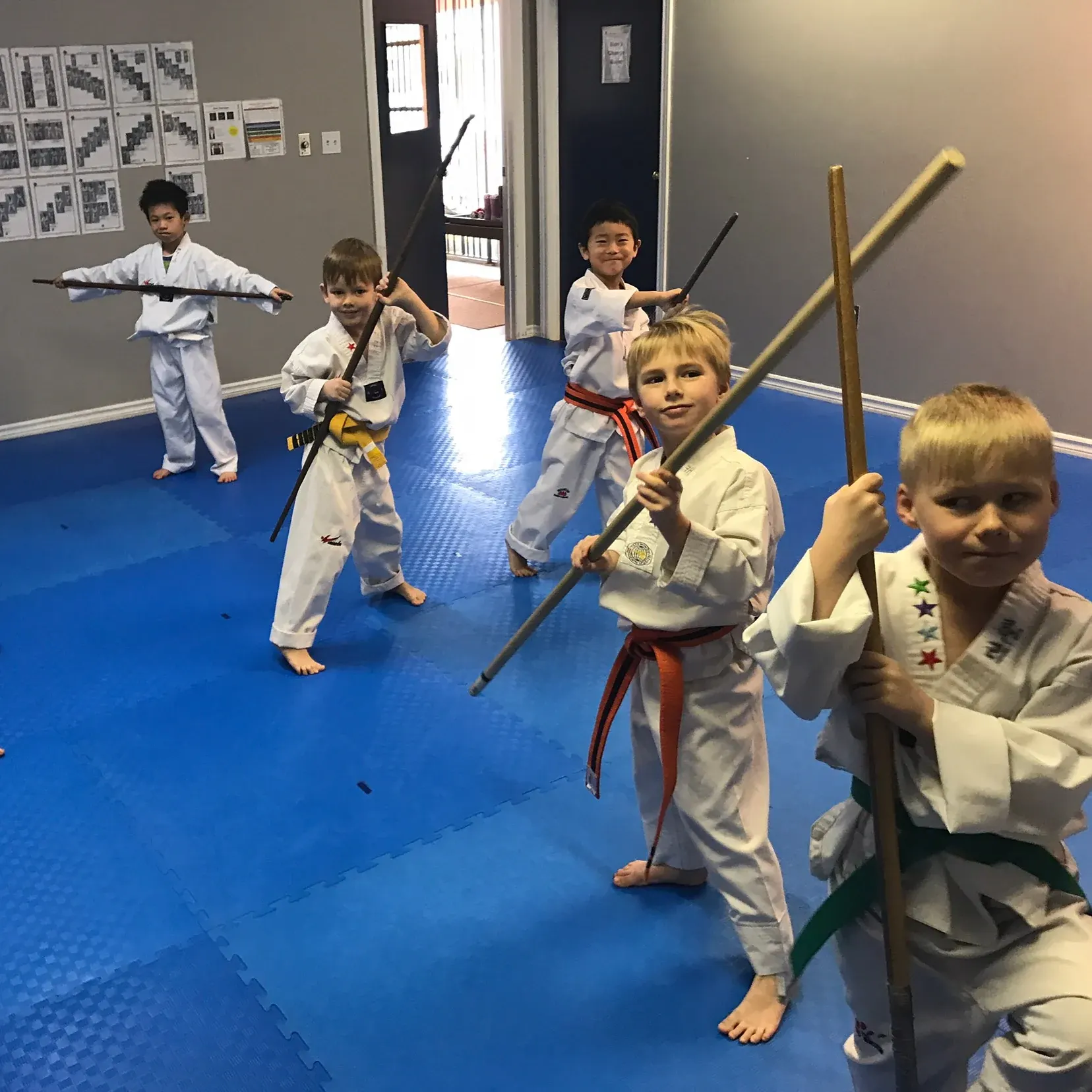 Children in uniforms practise with bo staffs on the mat