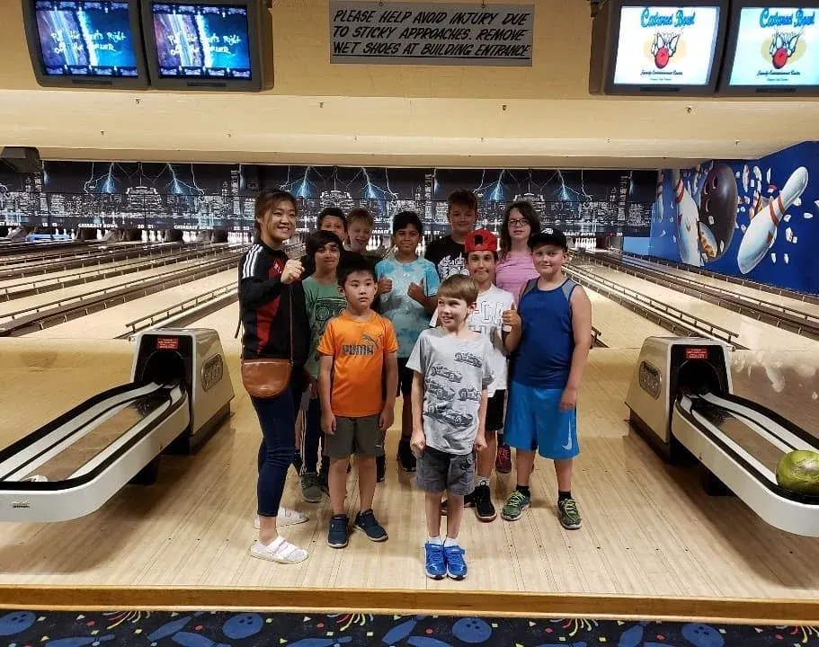 A group of campers stands in front of the lanes at a bowling alley