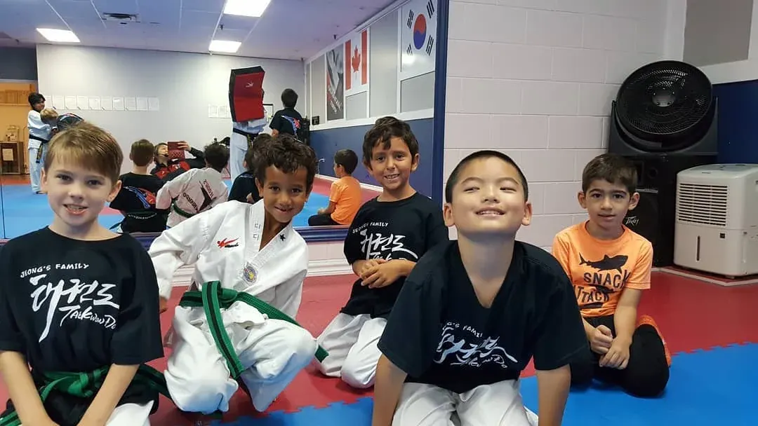 Five children, most in Jeong's t-shirts, smile on the mat