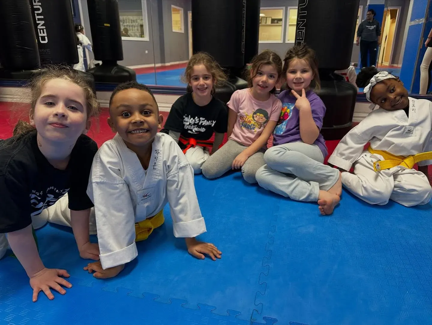 Children sit close together on the mat and smile at the camera