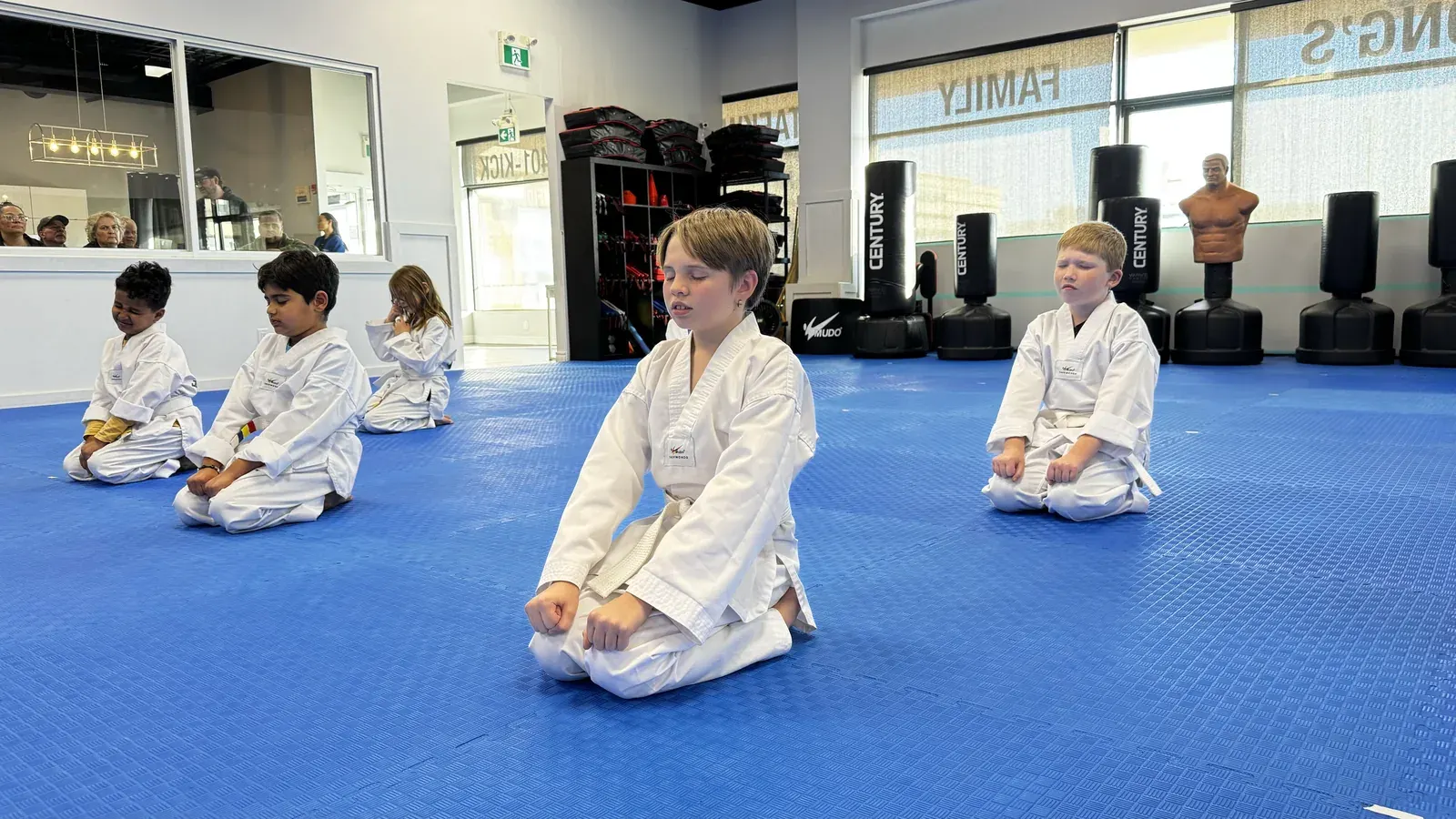 Children in white uniforms kneel in a row on the blue mats at the Niagara Falls school