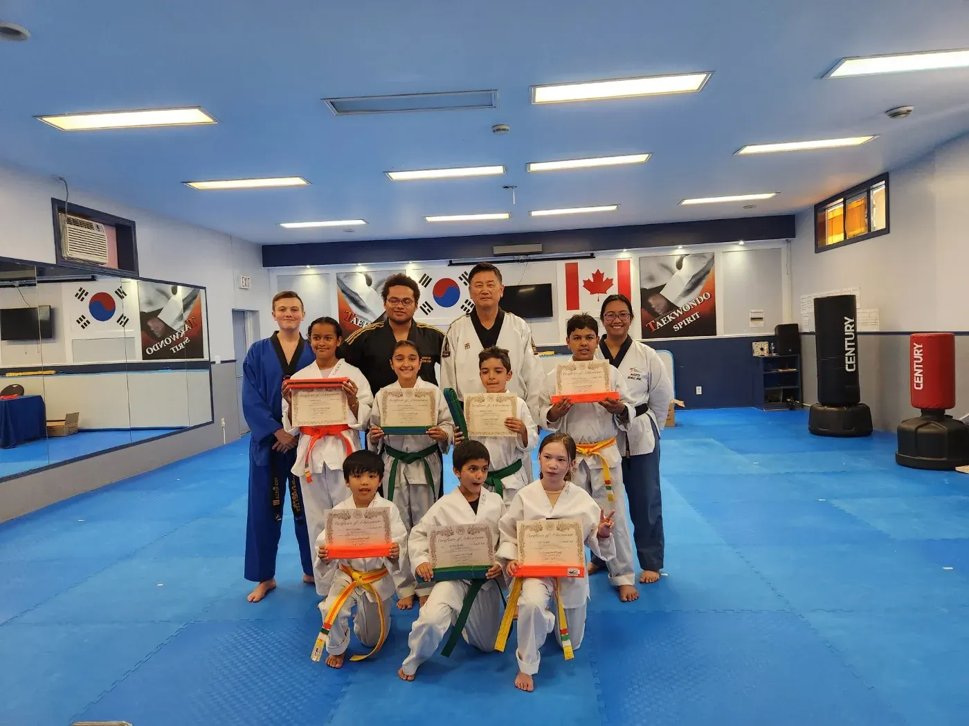 Students in yellow, orange and green belts show their certificates after a belt test, with their instructors