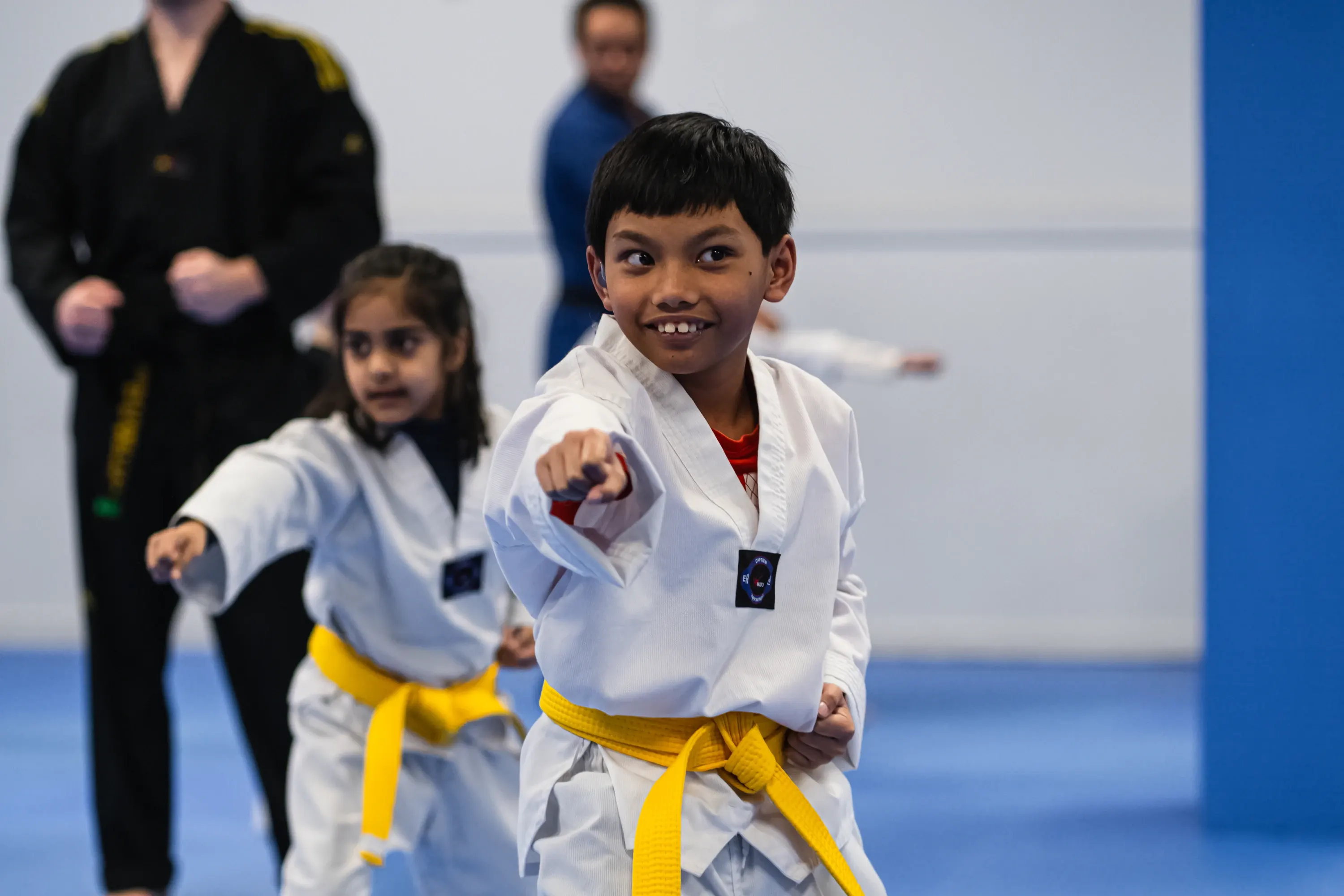 A smiling boy in a yellow belt throws a punch in class, with a classmate and two instructors behind him