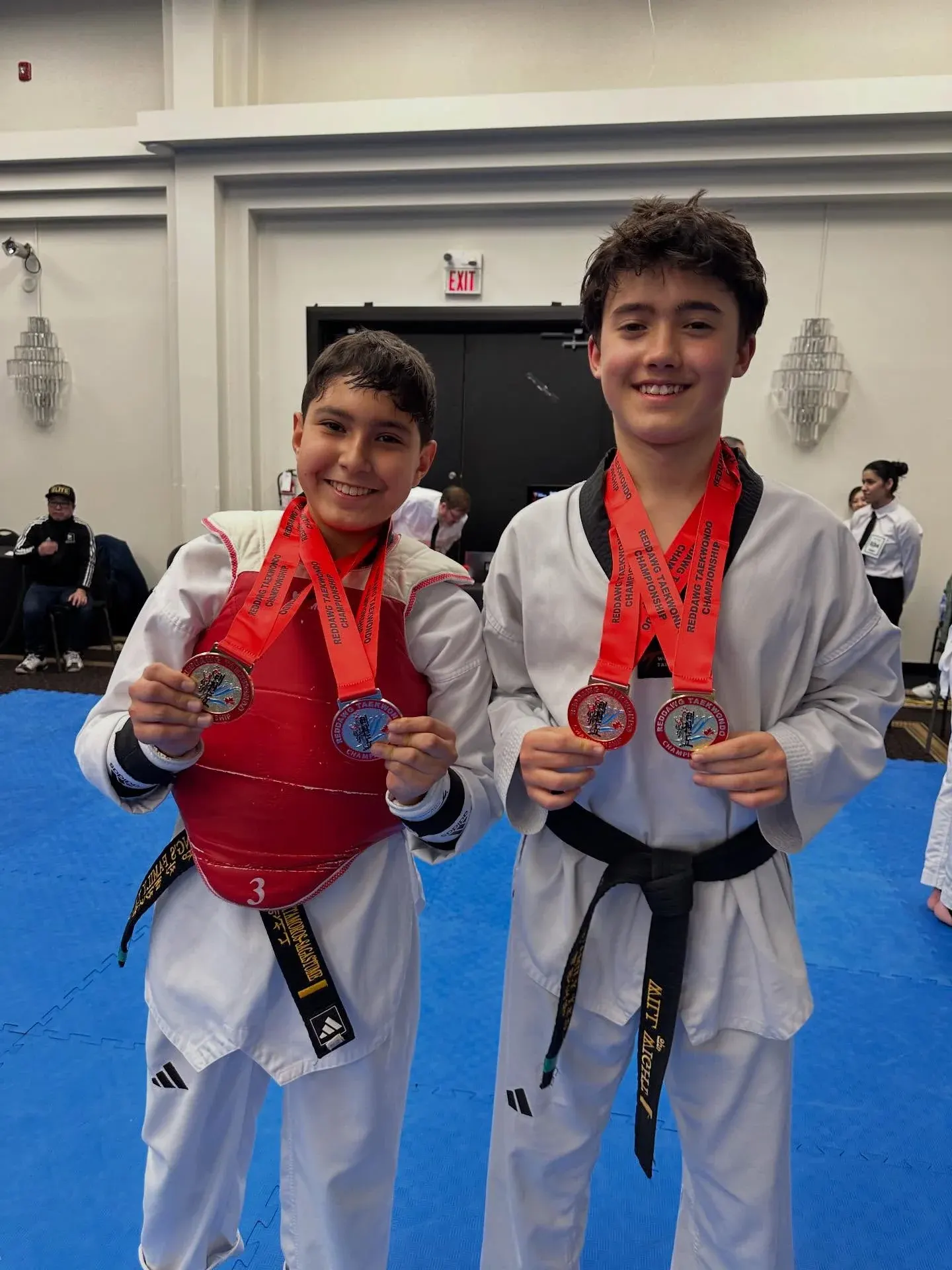 Two High Performance students in sparring gear show their medals at a tournament