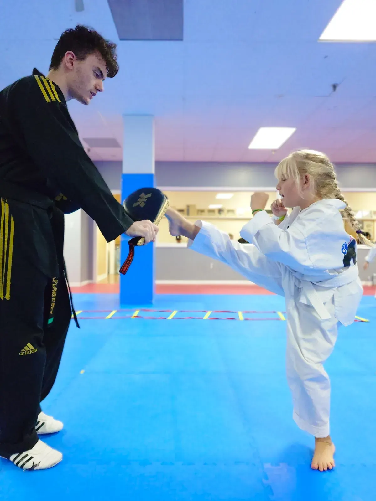 A young student kicks a pad held by her instructor