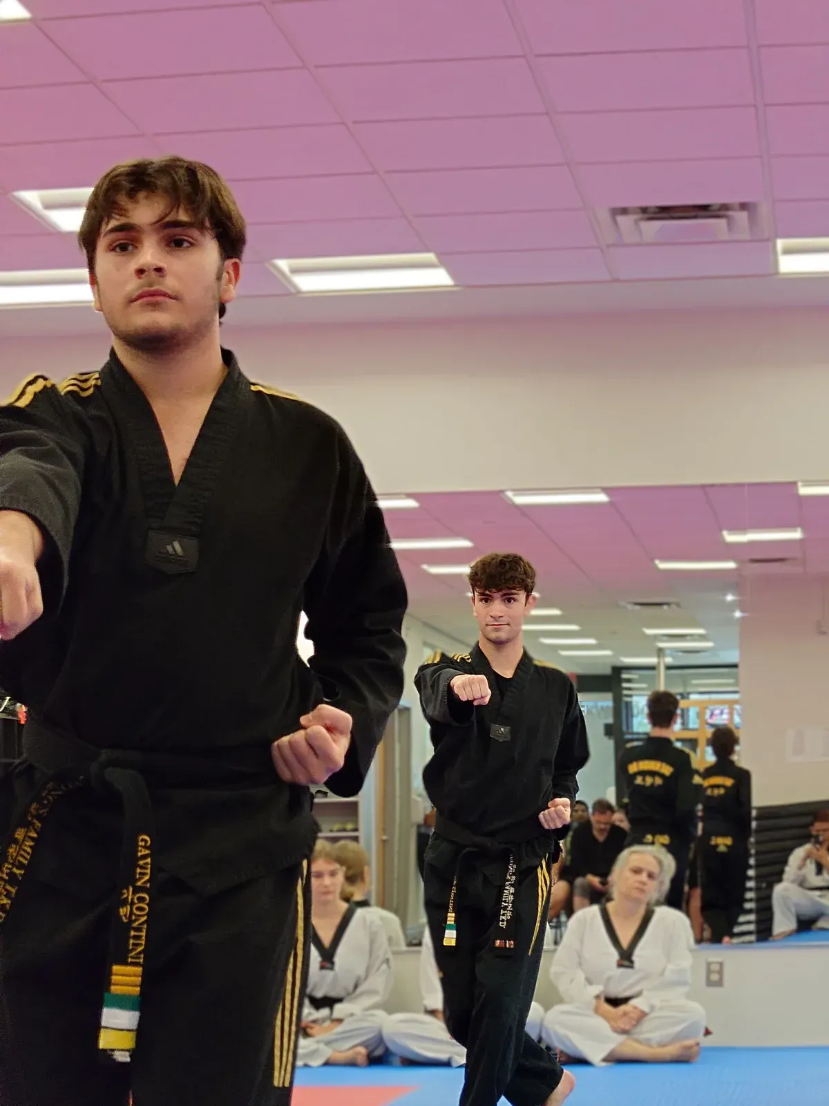 Black belts in black uniforms practise their punches while students sit and watch
