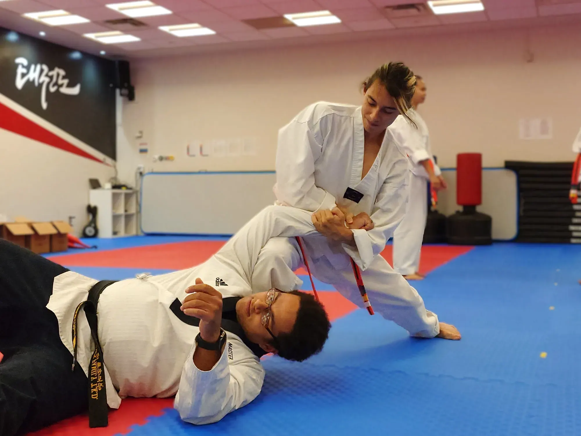 An adult student pins a master to the mat during a self-defence drill
