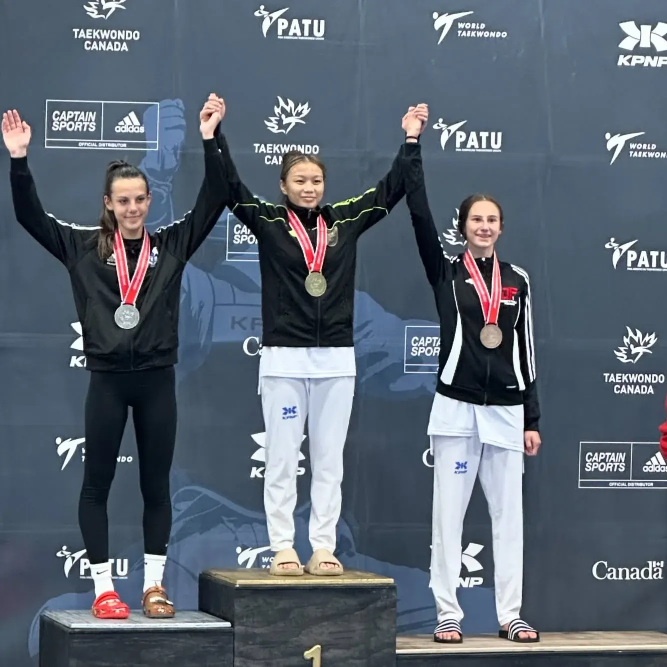 Three athletes with their medals on a Taekwondo Canada podium, Violet Yerich among them